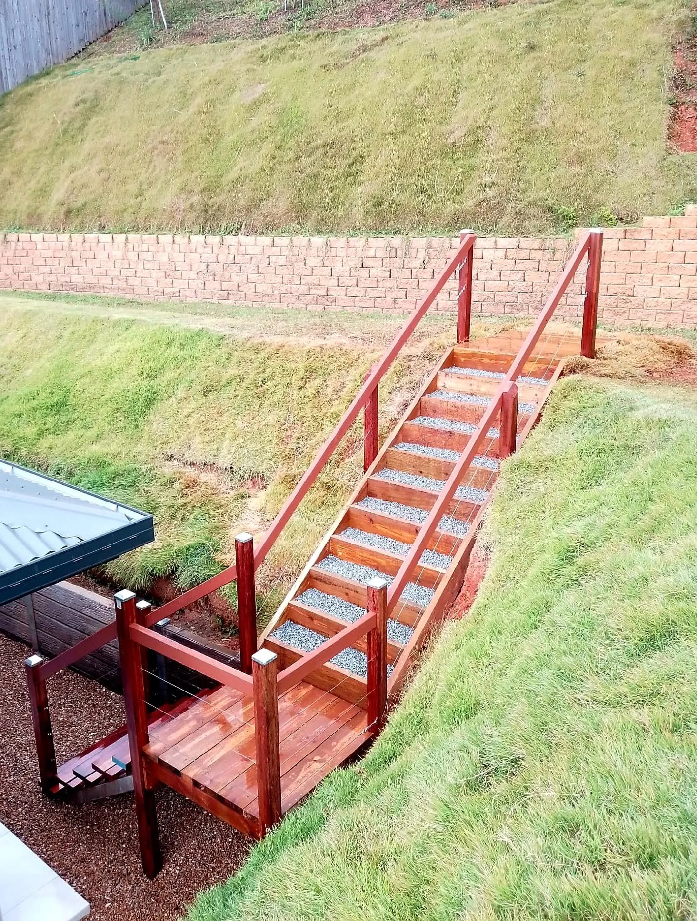 Timber staircase with handrail built down a grassed slope beside a block retaining wall