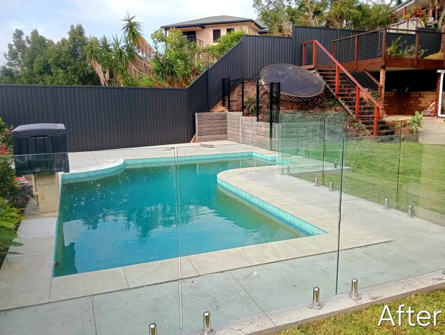 Swimming pool with frameless glass fencing, paved surround and landscaped garden