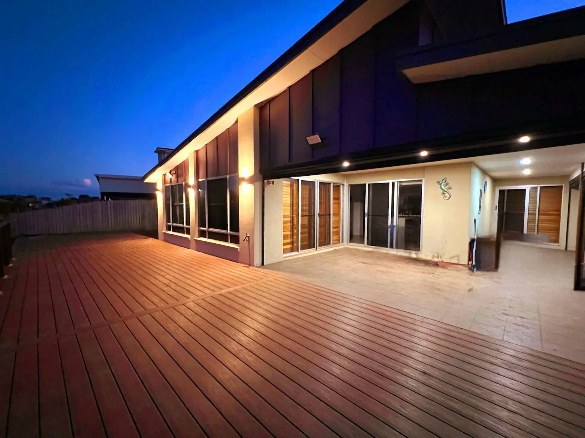 Large timber deck lit at dusk alongside a modern home